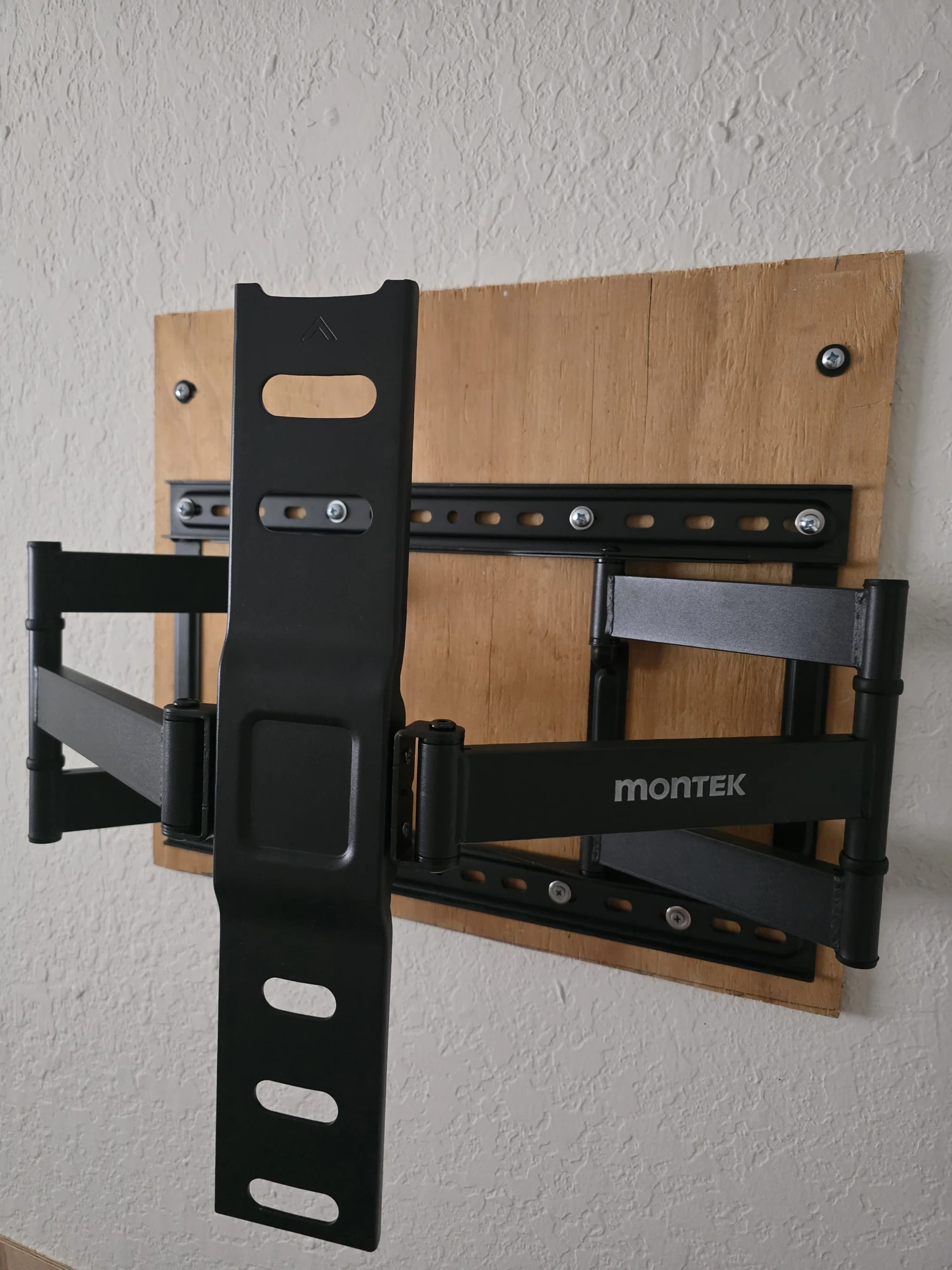 Full-motion TV bracket mounted over plywood backing on a textured white wall