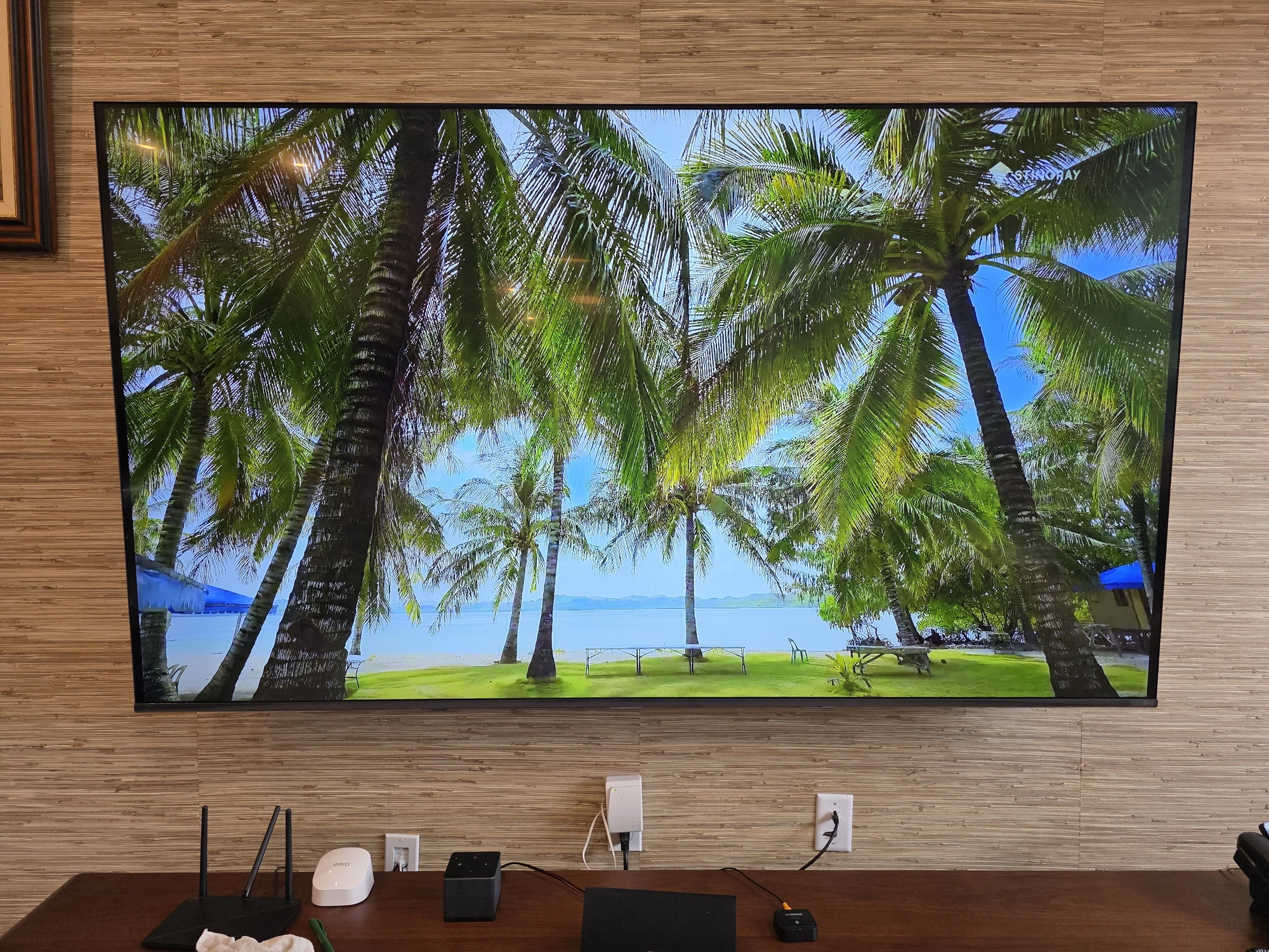 Large wall-mounted TV showing a tropical scene on an existing textured feature wall