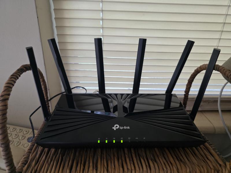 TP-Link router on a shelf beside window blinds